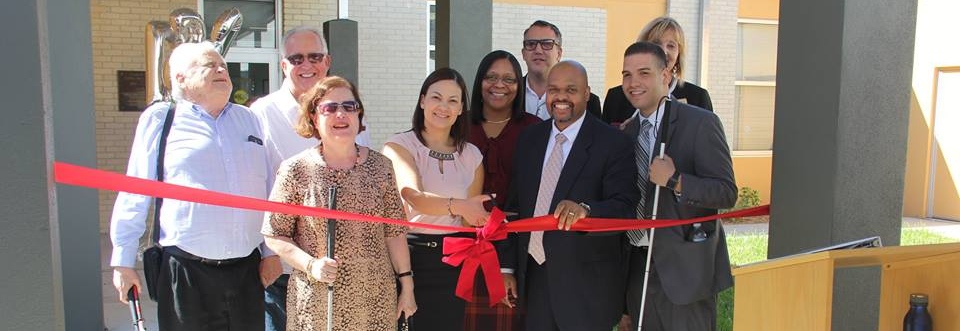 Members of the Florida Rehabilitation Council for the Blind, DBS staff, and others cut a large red ribbon outside of the newly re-opened DBS district office in Tampa.